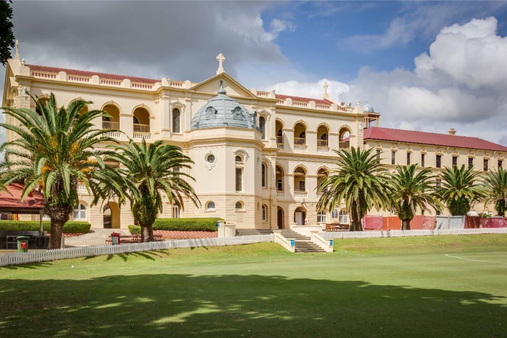 A large, grand classical building with a dome, viewed from a green oval.