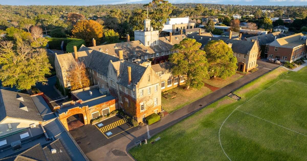 Aerial view of stone school buildings and a green sports oval